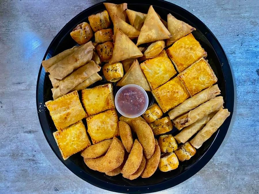 Savoury platter with samoosas, spring rolls, sausage rolls, pies and crumbed half moons around a dipping sauce